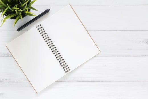 Image of a notepad open on  a white wooden table with a pen and plant