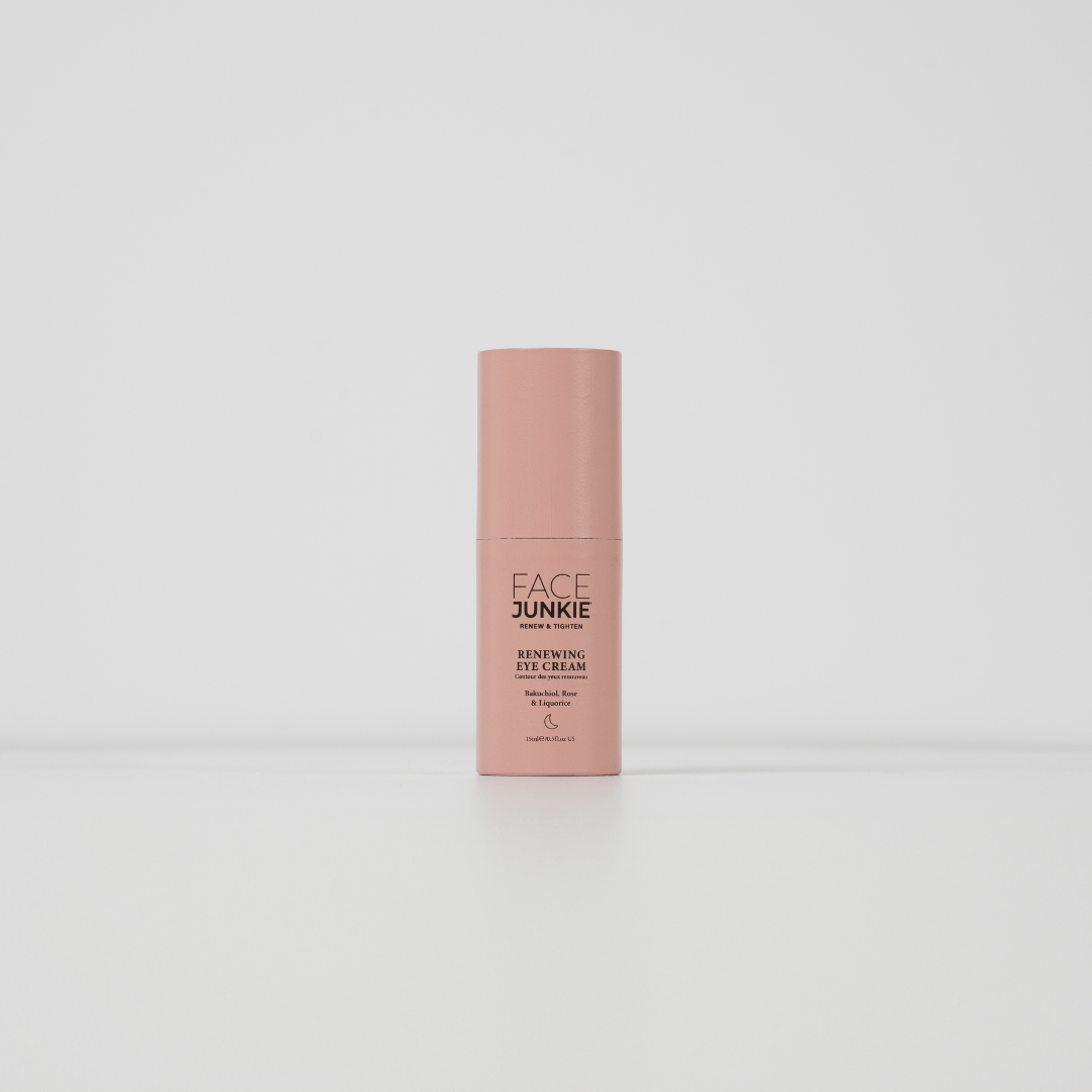 The image displays a single bottle of a skincare product standing upright against a plain white background. The product is labeled &quot;FACE JUNKIE Renewing Eye Cream,&quot; and the bottle is a soft pink color with a minimalist design. The text on the bottle mentions that the cream contains beneficial ingredients like Bakuchiol, Rose, and Caffeine, intended for eye care. The packaging is sleek and simple, creating a clean and modern aesthetic.