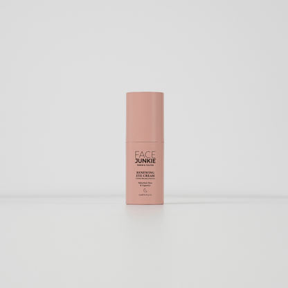 The image displays a single bottle of a skincare product standing upright against a plain white background. The product is labeled &quot;FACE JUNKIE Renewing Eye Cream,&quot; and the bottle is a soft pink color with a minimalist design. The text on the bottle mentions that the cream contains beneficial ingredients like Bakuchiol, Rose, and Caffeine, intended for eye care. The packaging is sleek and simple, creating a clean and modern aesthetic.